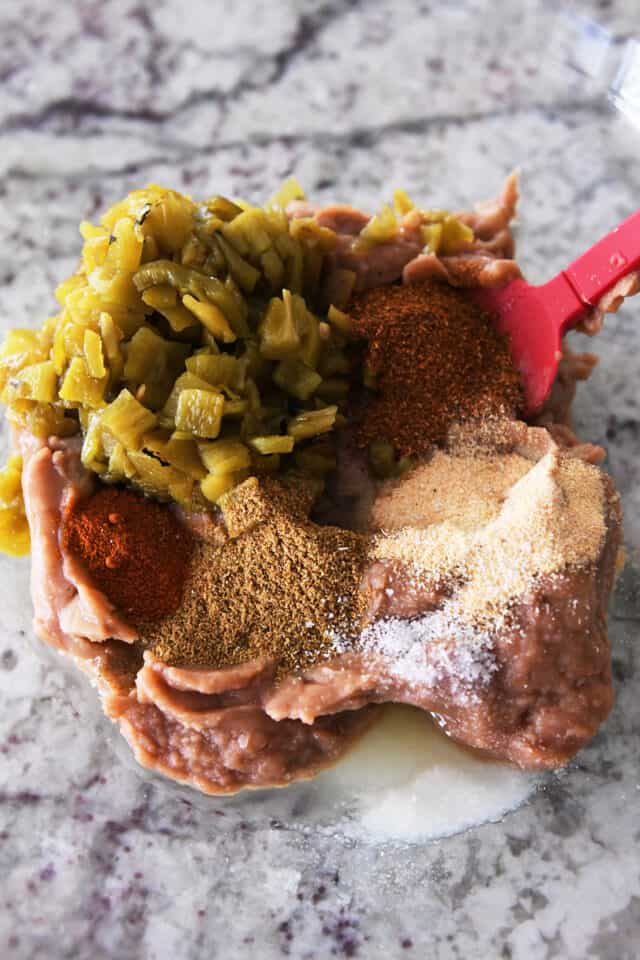 Refried beans, green chiles, chili powder, cumin, paprika and salt in glass bowl.