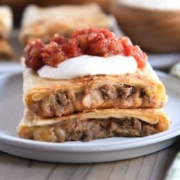 Two half beef and bean wraps on gray plate with salsa and sour cream.