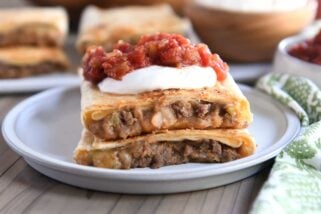 Two half beef and bean wraps on gray plate with salsa and sour cream.