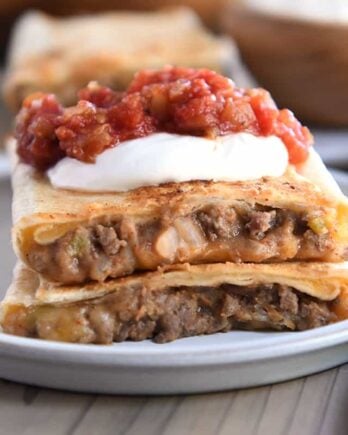 Two half beef and bean wraps on gray plate with salsa and sour cream.