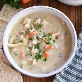 Top down view of creamy chicken noodle soup with saltine crackers on the side.