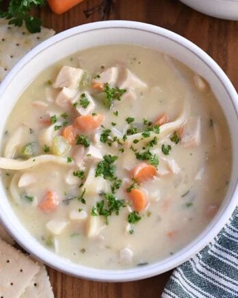 Top down view of creamy chicken noodle soup with saltine crackers on the side.