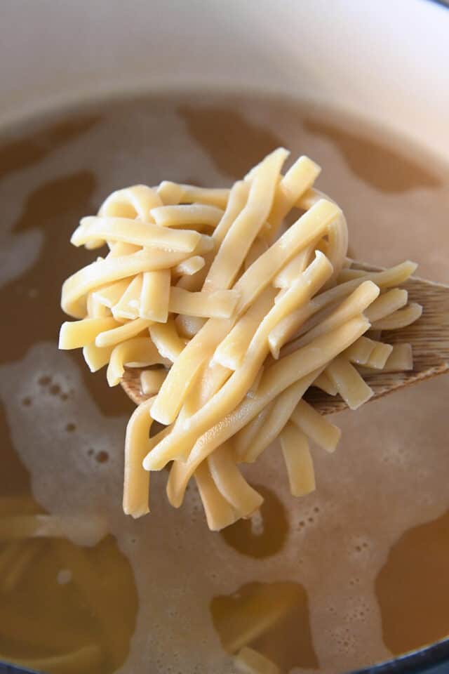 Wooden spoon full of thick frozen noodles.