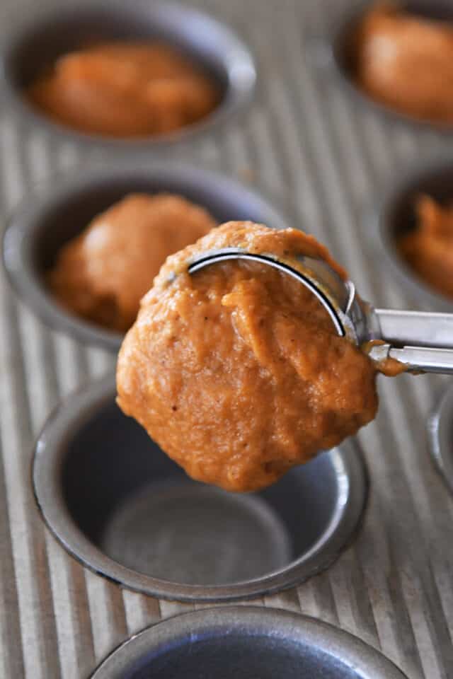 Using cookie scoop to portion pumpkin muffin batter in mini muffin tin.