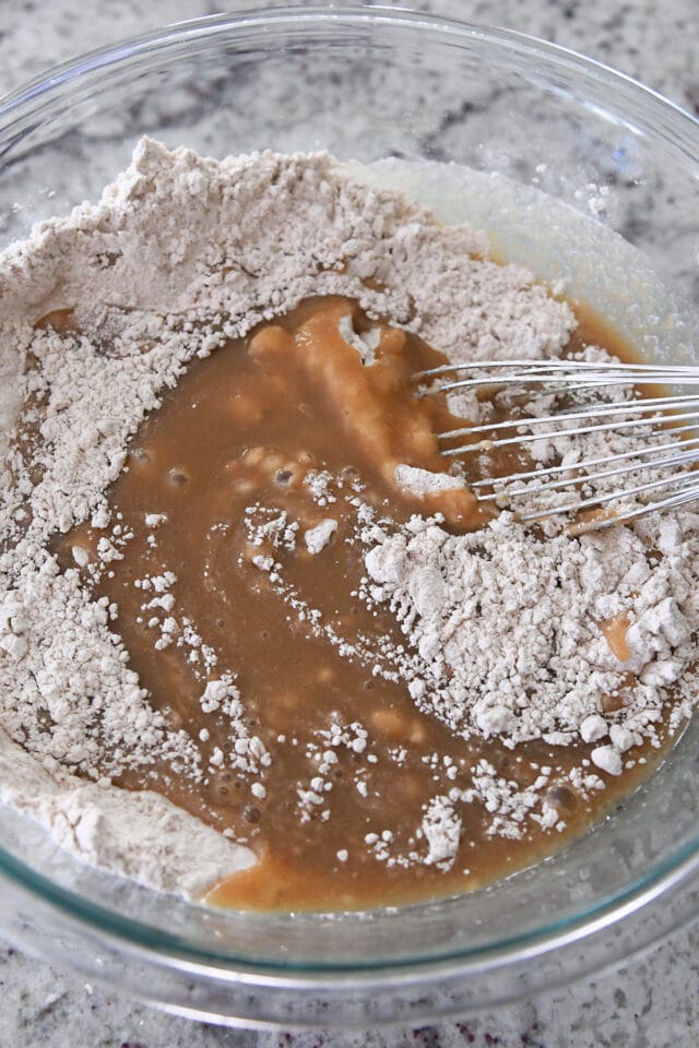 Glass bowl with whisk mixing dry ingredients into wet ingredients for applesauce spice cake.