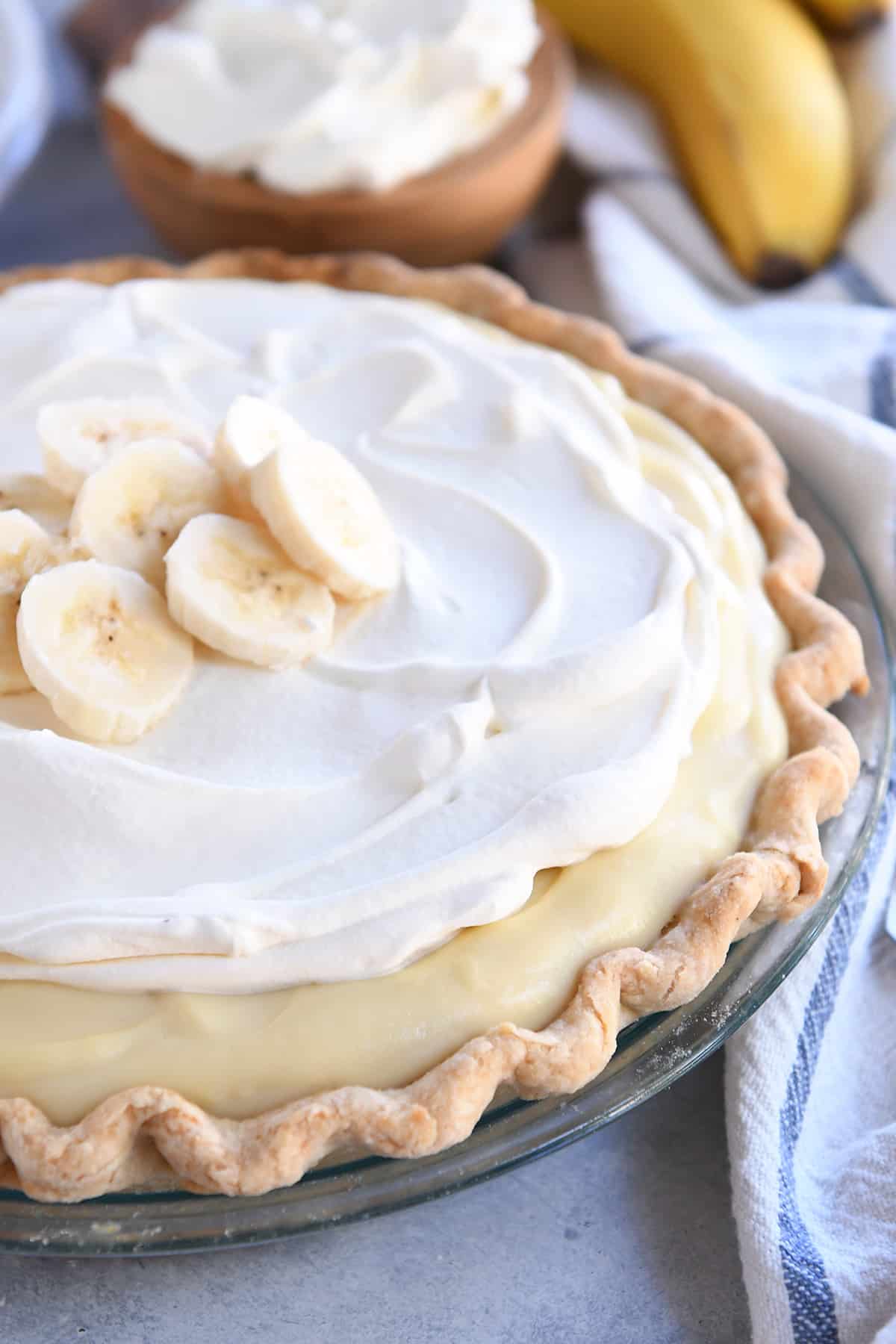 Whole banana cream pie topped with sliced bananas and whipped cream.