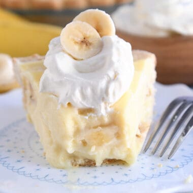 Bite taken out of piece of banana cream pie on white plate.