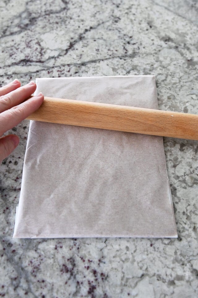 Rolling out cinnamon sugar ،er packet in parchment paper with rolling pin.