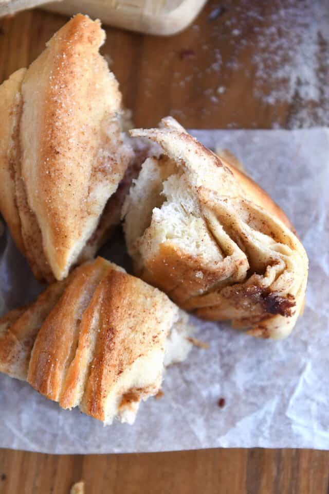 Several torn pieces of croissant bread with cinnamon sugar on parchment paper.