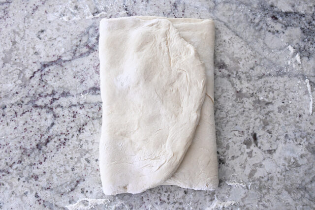 French bread dough folded into thirds on floured counter.