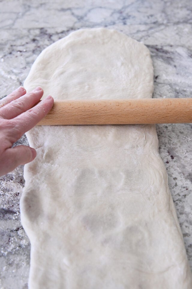 Rolling croissant bread dough into very long rectangle.
