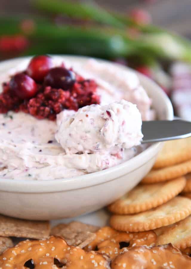 Small knife lifting scoop of cranberry jalapeno dip out of white bowl.