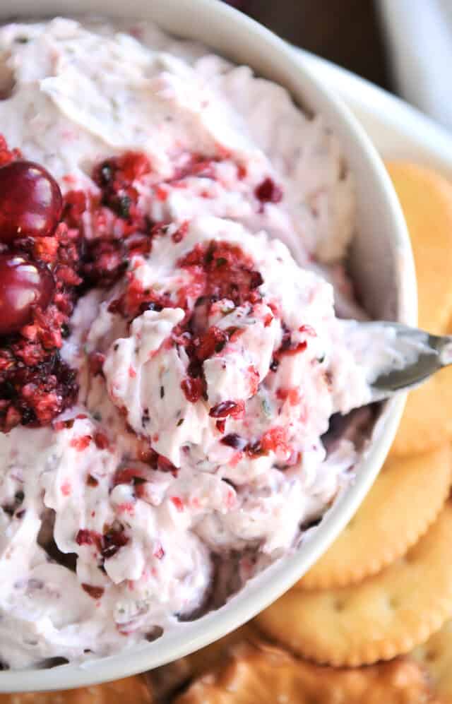 White bowl with small knife lifting scoop of cranberry jalapeño dip.