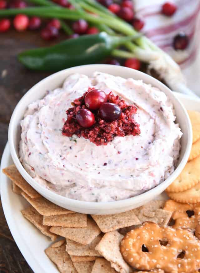 Cream bowl filled with cranberry jalapeno dip and fresh cranberries on top.