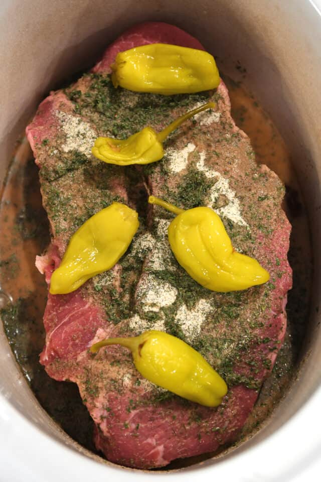 Chuck roast in slow cooker insert with pepperoncini, seasonings and beef broth.