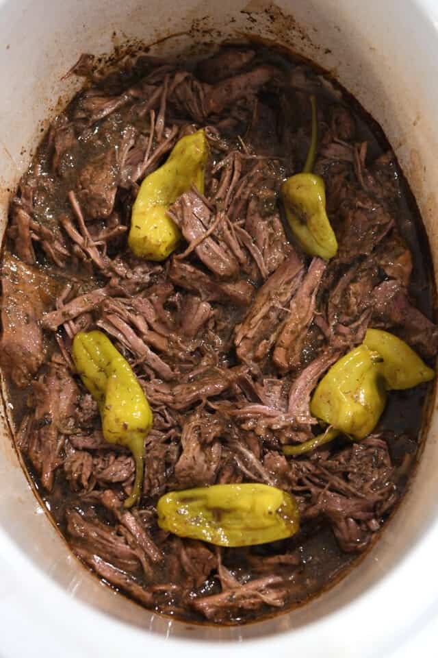 Shredded beef in slow cooker with gravy and pepperoncini.