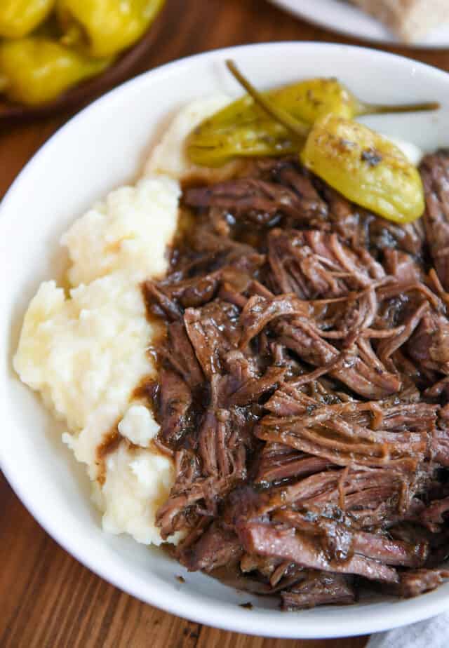 White bowl with mashed potatoes, shredded beef and gravy, and pepperoncini.