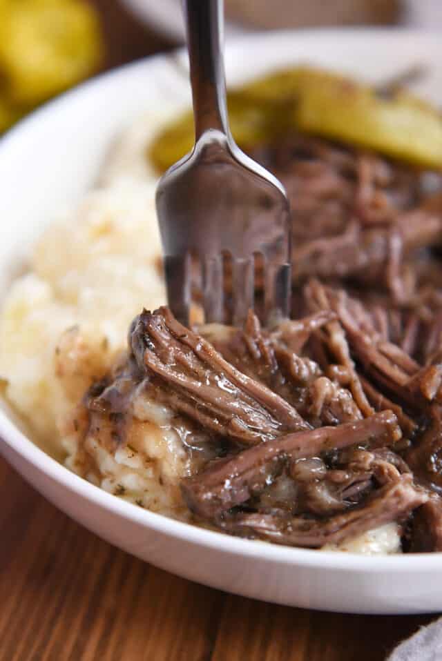 Fork taking bite of mashed potatoes, shredded beef and gravy.