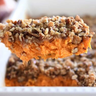 Serving spoon with sweet potato casserole and pecan topping.
