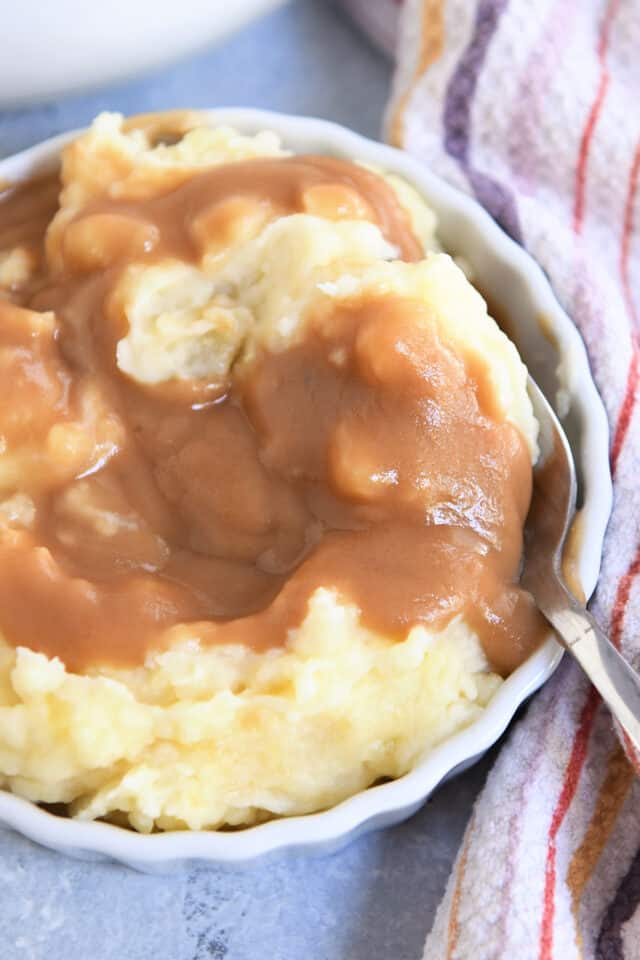 White dish with mashed potatoes, brown gravy and spoon.