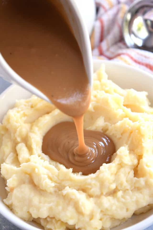 Pouring gravy from gravy boat onto mashed potatoes.