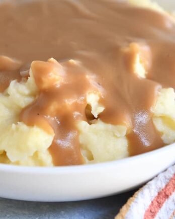 White bowl with mashed potatoes and brown gravy.
