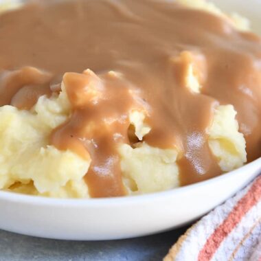 White bowl with mashed ،atoes and brown gravy.