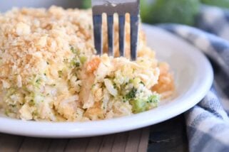 Fork scooping bite of casserole on white plate with rice, broccoli and carrots.