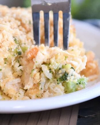 Fork scooping bite of casserole on white plate with rice, broccoli and carrots.