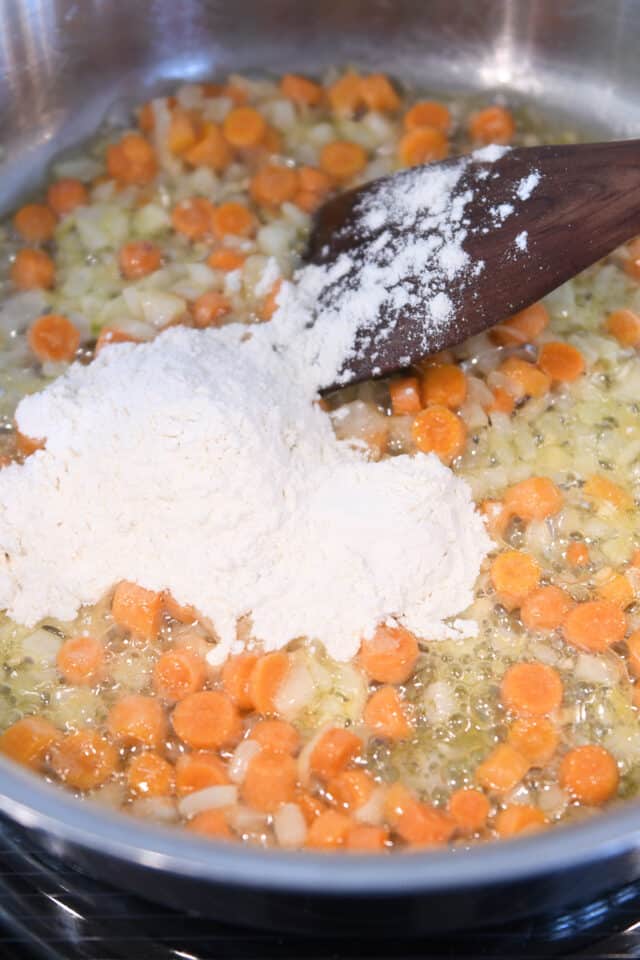 Adding flour to skillet with butter and carrots for roux.
