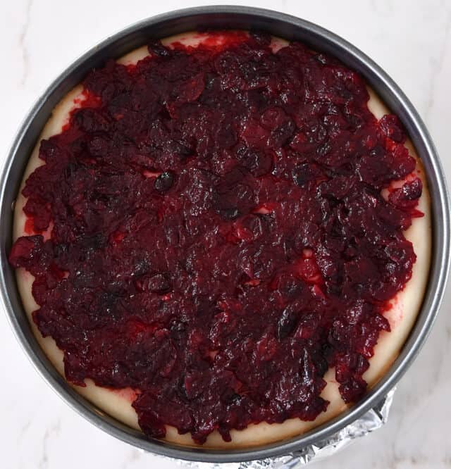 Cranberry jam spread over baked cheesecake in springform pan.