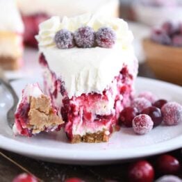 Slice of cranberry white chocolate mousse cheesecake on white plate with bite taken out.