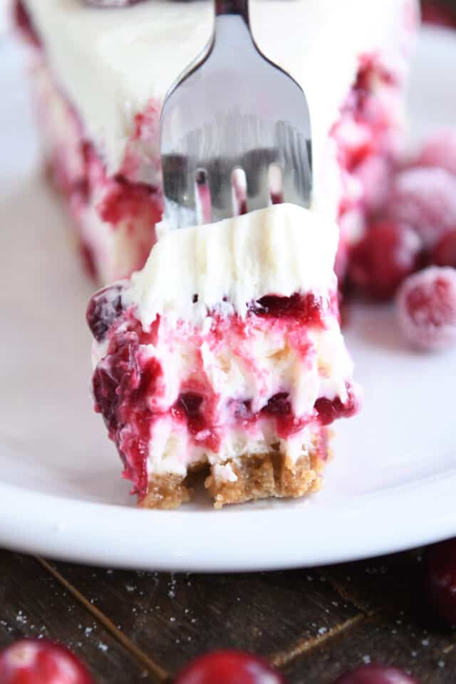 Piece of cranberry cheesecake on fork on white plate.