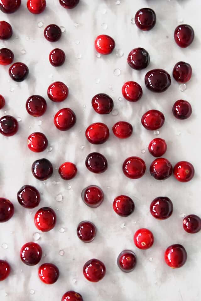 Fresh cranberries covered in simple syrup on parchment lined baking pan.