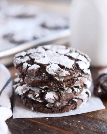 Four chocolate crinkle cookies stacked on parchment paper.