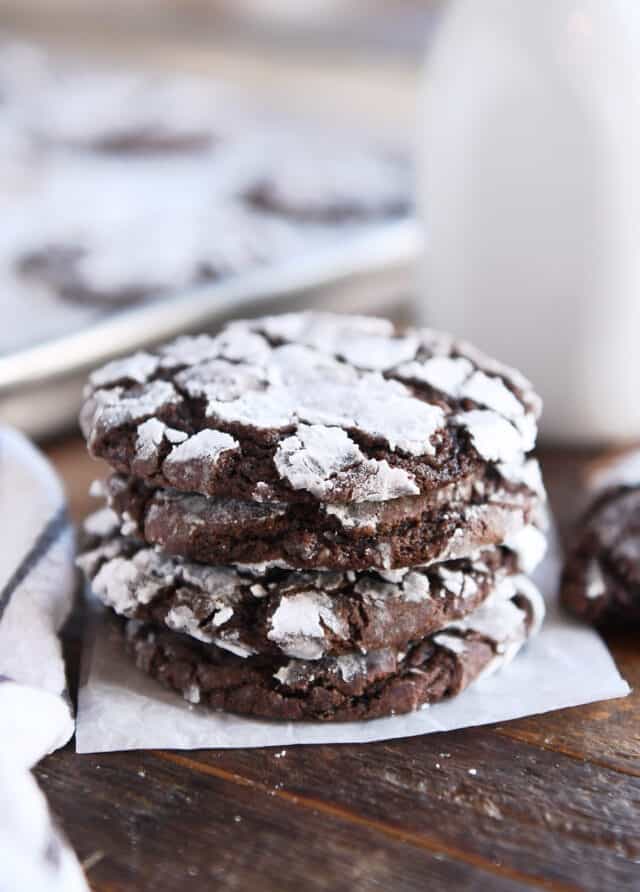 Four chocolate crinkle cookies stacked on parchment paper.