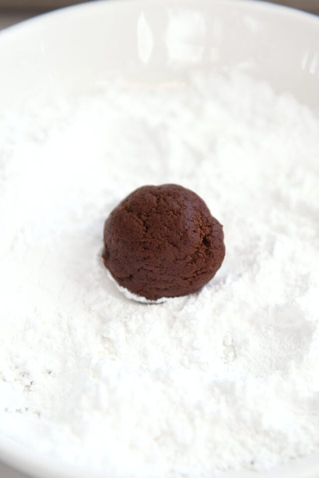 Chocolate cookie dough ball in bowl of powdered sugar.