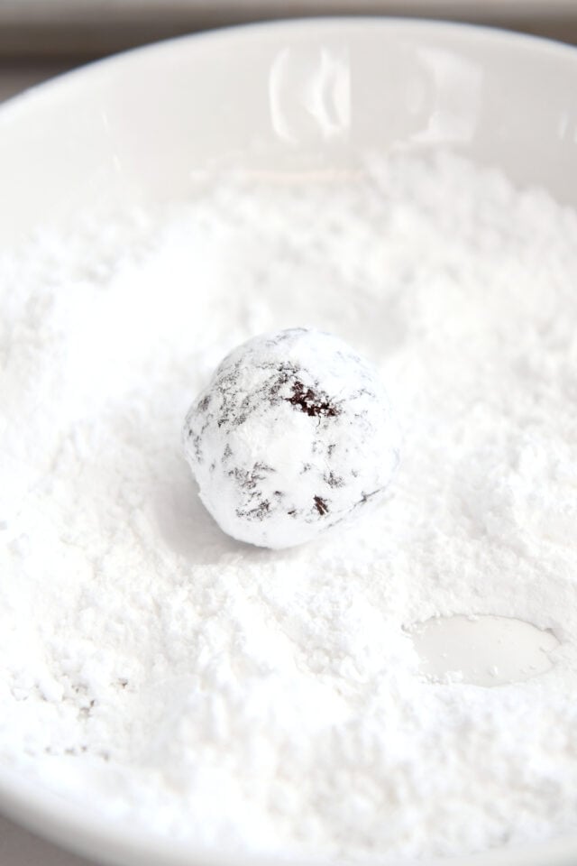 Rolling chocolate cookie dough ball in powdered sugar.