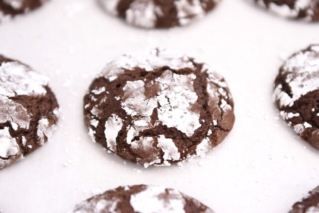 Several chocolate crinkle cookies on parchment paper.