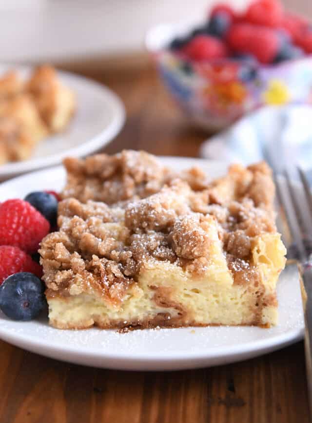 Square serving of French toast bake on white plate with fresh berries and powdered sugar.