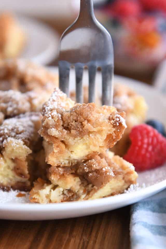 Fork skewering two bites of baked French toast on white plate.