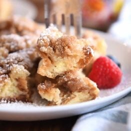 Fork skewering two bites of baked French toast on white plate.