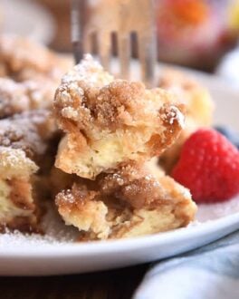 Fork skewering two bites of baked French toast on white plate.