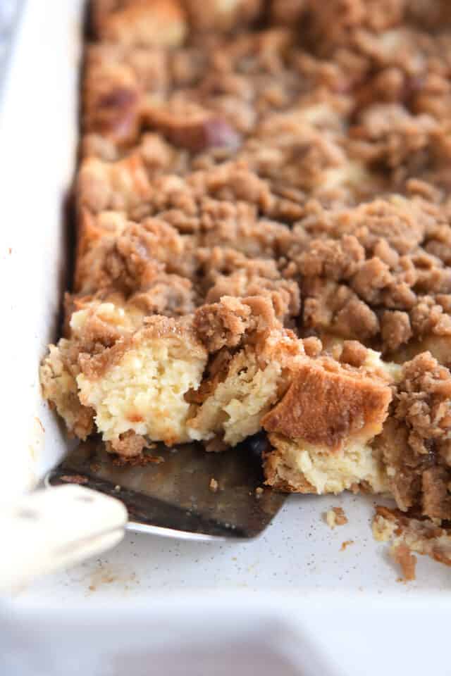 Spatula scooping up French toast bake in white pan.