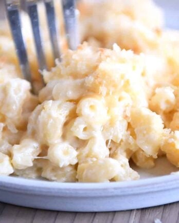 Fork taking bite of macaroni and cheese on gray plate.