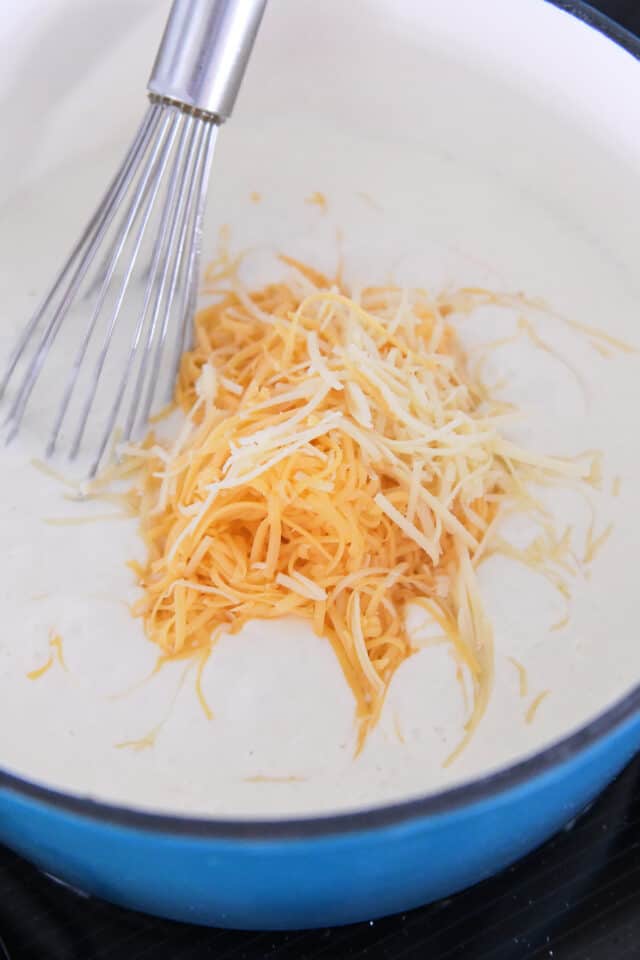 Adding shredded cheese to white sauce.
