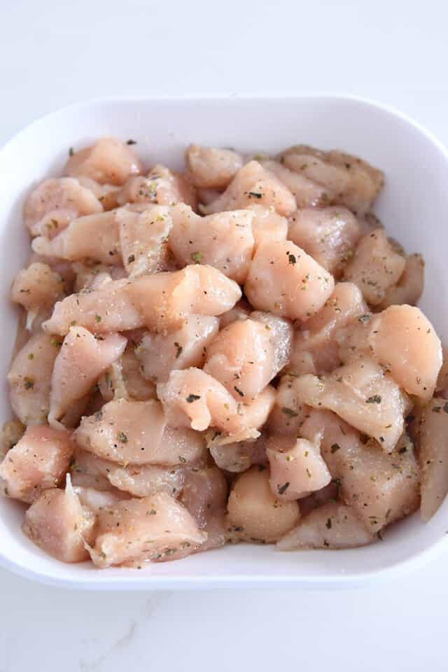 Cubed chicken in white bowl with basil, oregano and thyme.