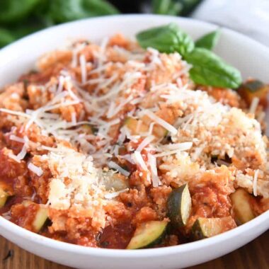 Serving of chicken zucchini Italian skillet in white bowl with parmesan cheese and fresh basil.