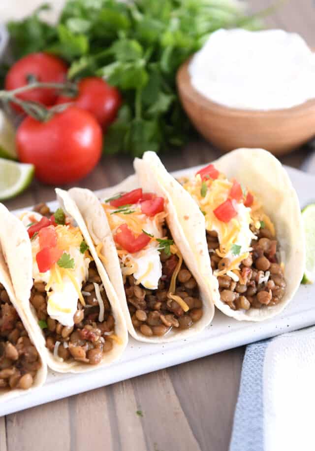 Three tacos of flour tortillas filled with cooked lentils, sour cream, cheese and tomatoes.