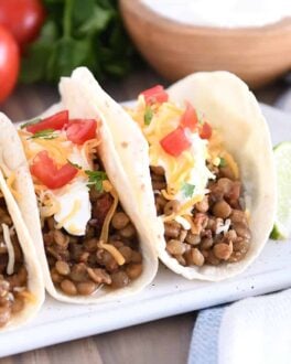 Three tacos of flour tortillas filled with cooked lentils, sour cream, cheese and tomatoes.